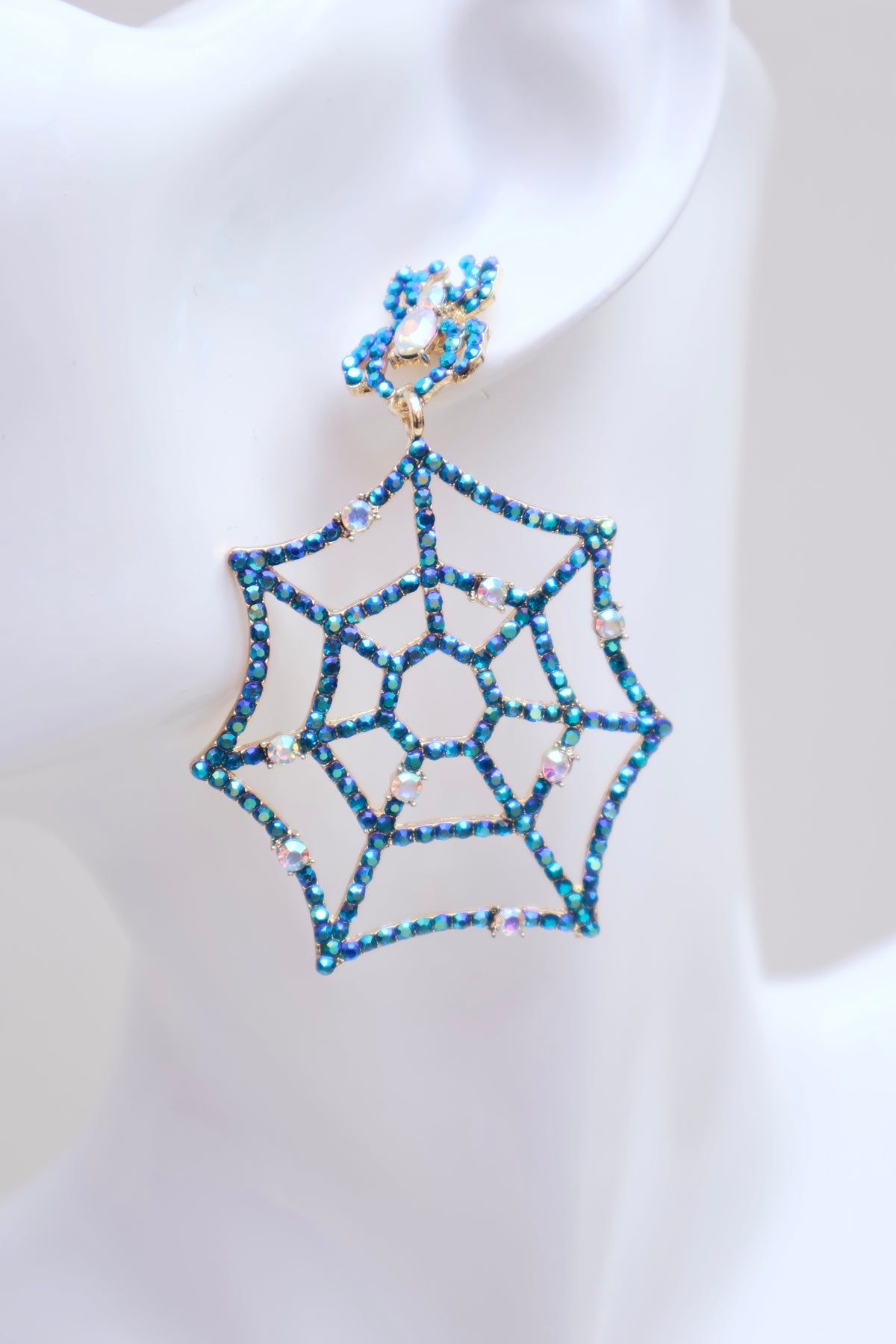 A single spiderweb-shaped drop earring with blue rhinestones and gold-tone metal, displayed on a white mannequin ear.