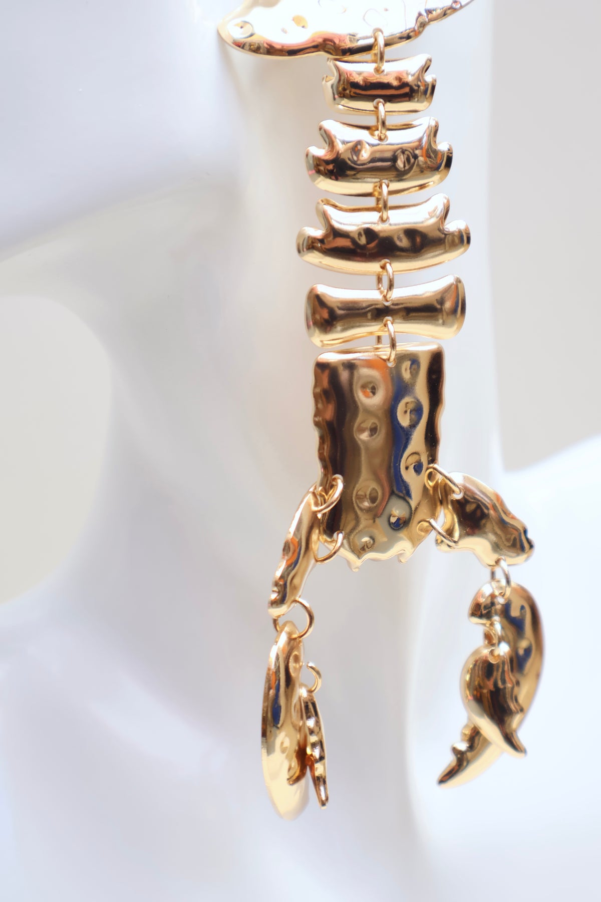 A gold-toned lobster claw earring displayed on a white mannequin bust. The earring features a lobster claw design with a hammered finish and dangling fish charms.